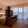 Modernes Hotelzimmer mit Doppelbett, Fernseher, Schreibtisch und gro&szlig;en Fenstern mit Vorh&auml;ngen.