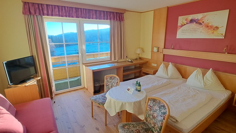 Gem&uuml;tliches Hotelzimmer mit Doppelbett, Tisch, St&uuml;hlen und Fernseher. Fenster mit Blick auf Berge.