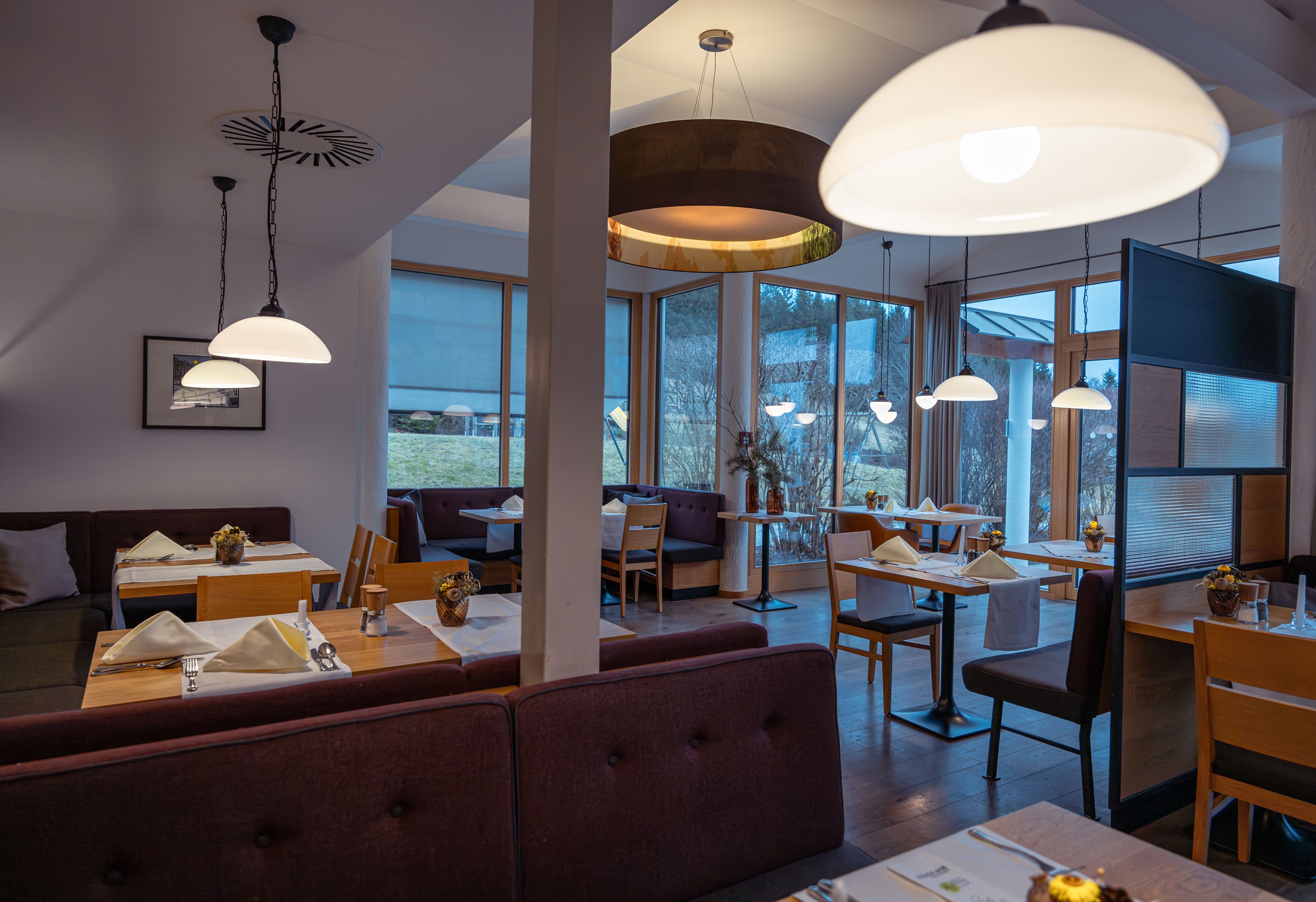 Innenansicht eines modernen Hotelrestaurants mit Holzmöbeln und großen Fenstern.