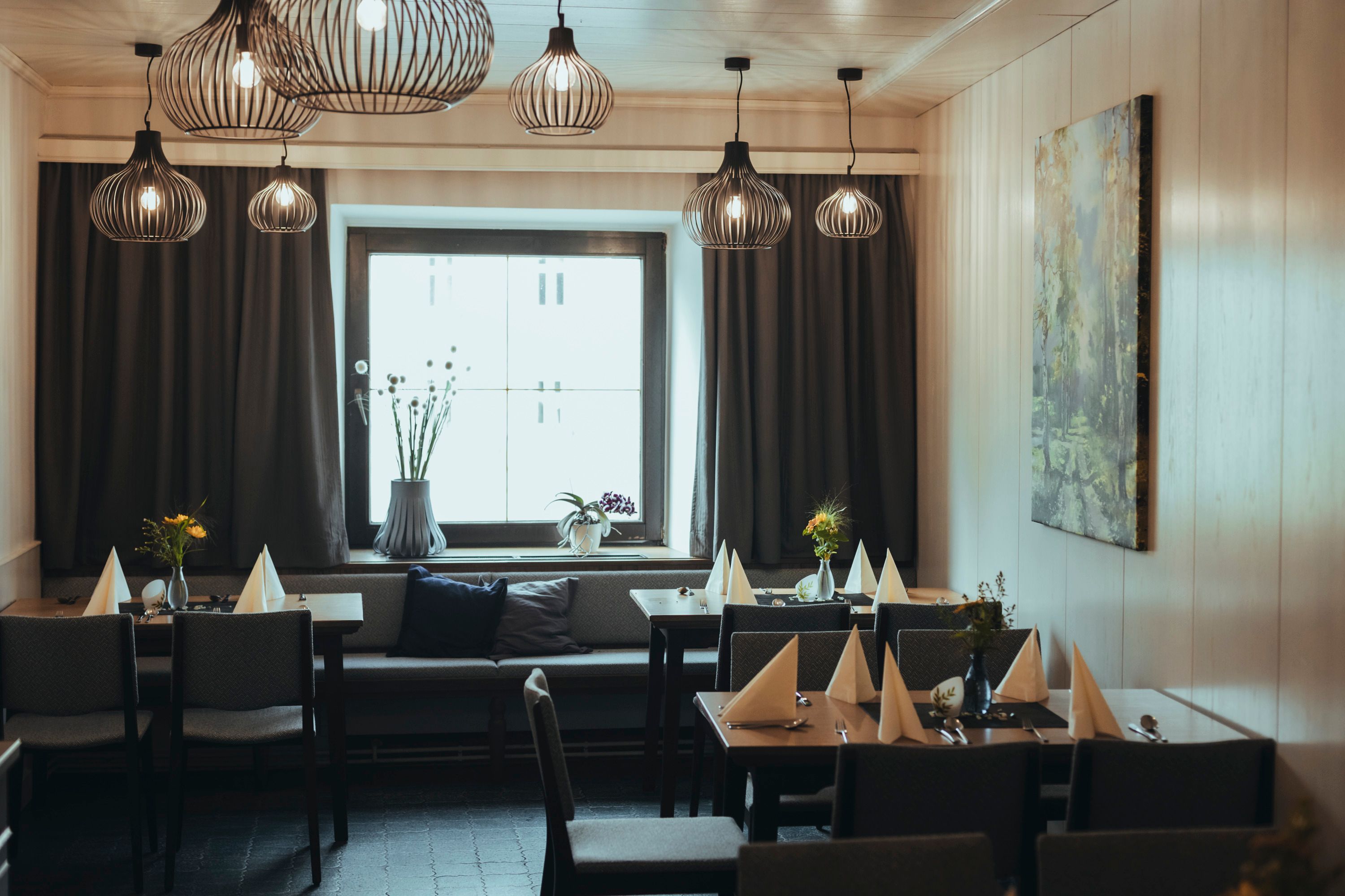 Modern eingerichtetes Gastzimmer mit stilvollen Lampen, gedeckten Tischen und einem großen Fenster.