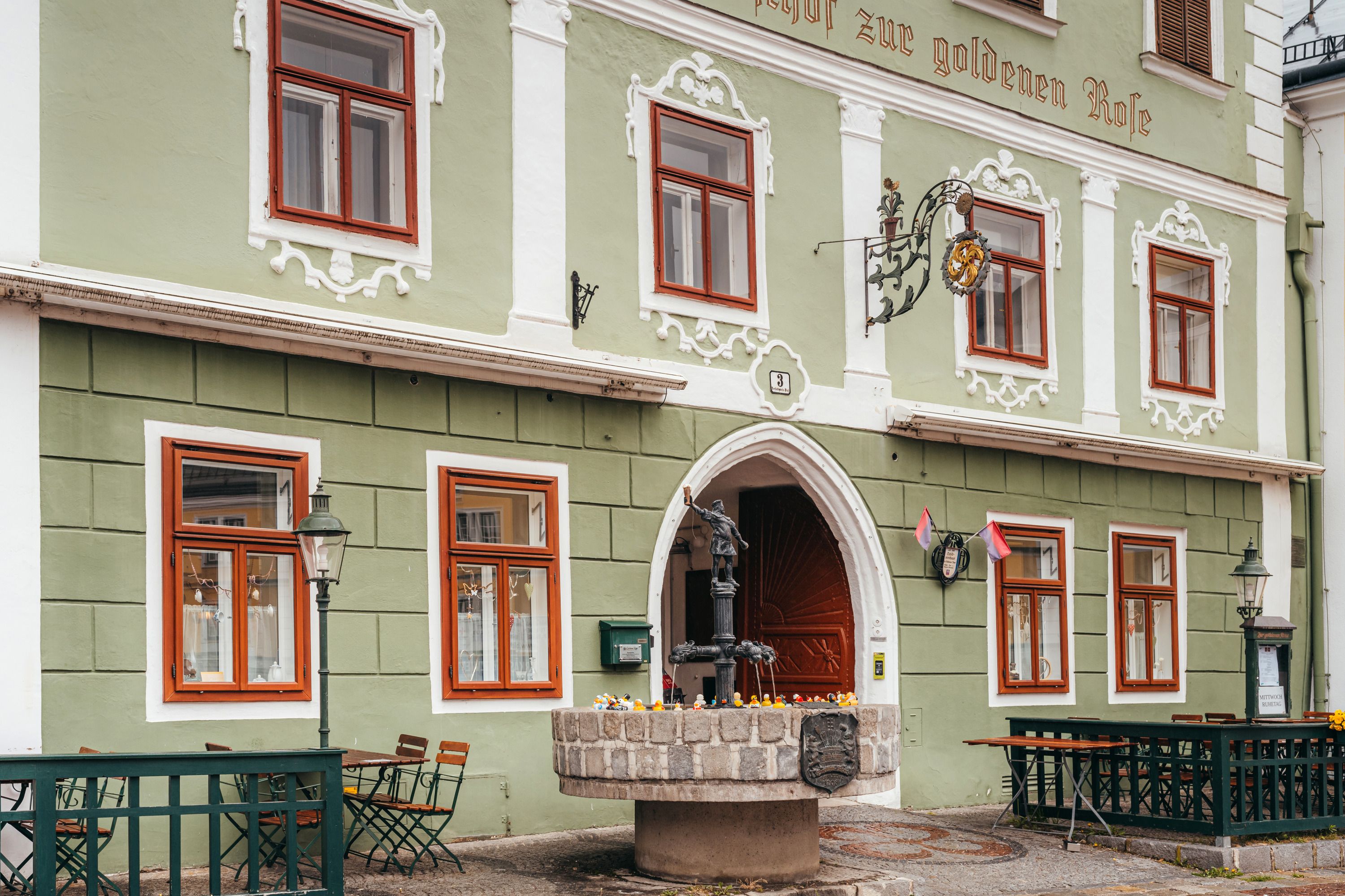Grünes Wirtshaus mit Bierbrunnen und Entenfiguren.