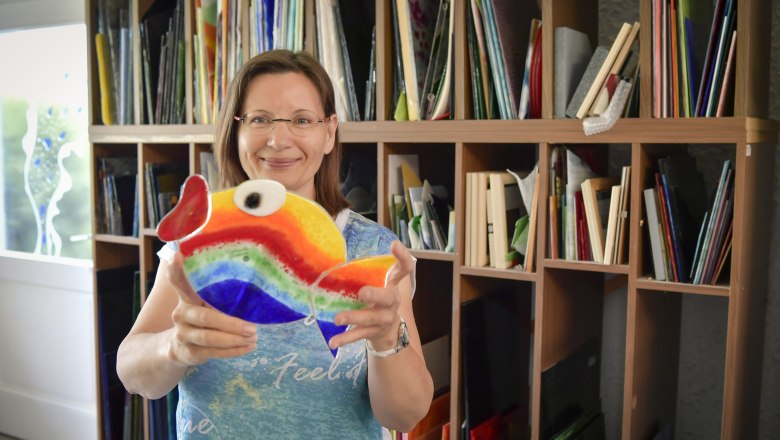 Frau h&auml;lt bunten Glasfisch in einem Atelier.