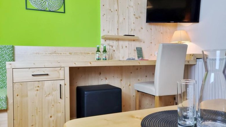 Ein Hotelzimmer mit Holzm&ouml;beln, einem Schreibtisch, einem Fernseher an der Wand und einer gr&uuml;nen Wanddekoration.