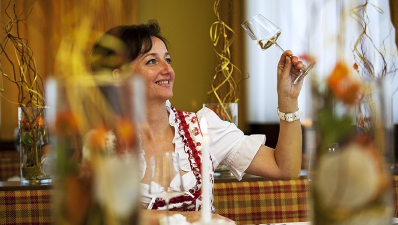 Frau in traditioneller Kleidung h&auml;lt ein Weinglas in einem Restaurant.