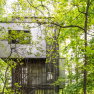 Modernes Baumhaus in einem dichten Wald, umgeben von gr&uuml;nen Bl&auml;ttern.