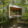 Modernes Baumhaus im Wald mit Balkon und Glasfront.