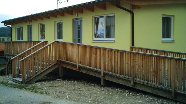 Gelbes Geb&auml;ude mit Holzrampe und Fenstern.