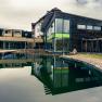 Modernes Wellnesshotel mit Holzfassade und gro&szlig;em Teich im Vordergrund.