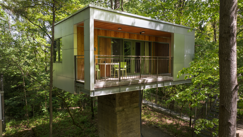 Modernes Baumhaus im Wald mit Balkon und Glasfront.