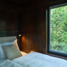 Innenansicht eines Baumhauses mit einem Bett und einem Fenster mit Blick auf den Wald.