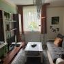 Gem&uuml;tliches Wohnzimmer mit Sofa, Couchtisch, Teppich und Fernseher. Ein Kronleuchter h&auml;ngt von der Decke, Pflanzen und Dekorationen sind sichtbar.