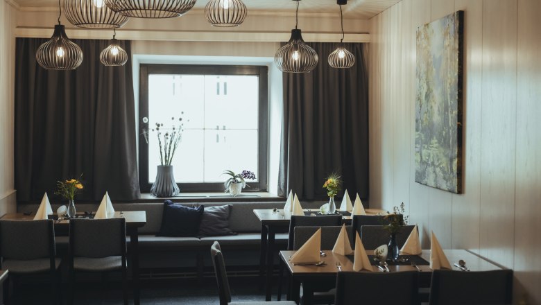 Modern eingerichtetes Gastzimmer mit stilvollen Lampen, gedeckten Tischen und einem gro&szlig;en Fenster.