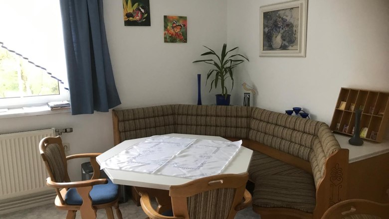 Eckbank in einer K&uuml;che mit Tisch und St&uuml;hlen, dekoriert mit Pflanzen und Bildern an der Wand.
