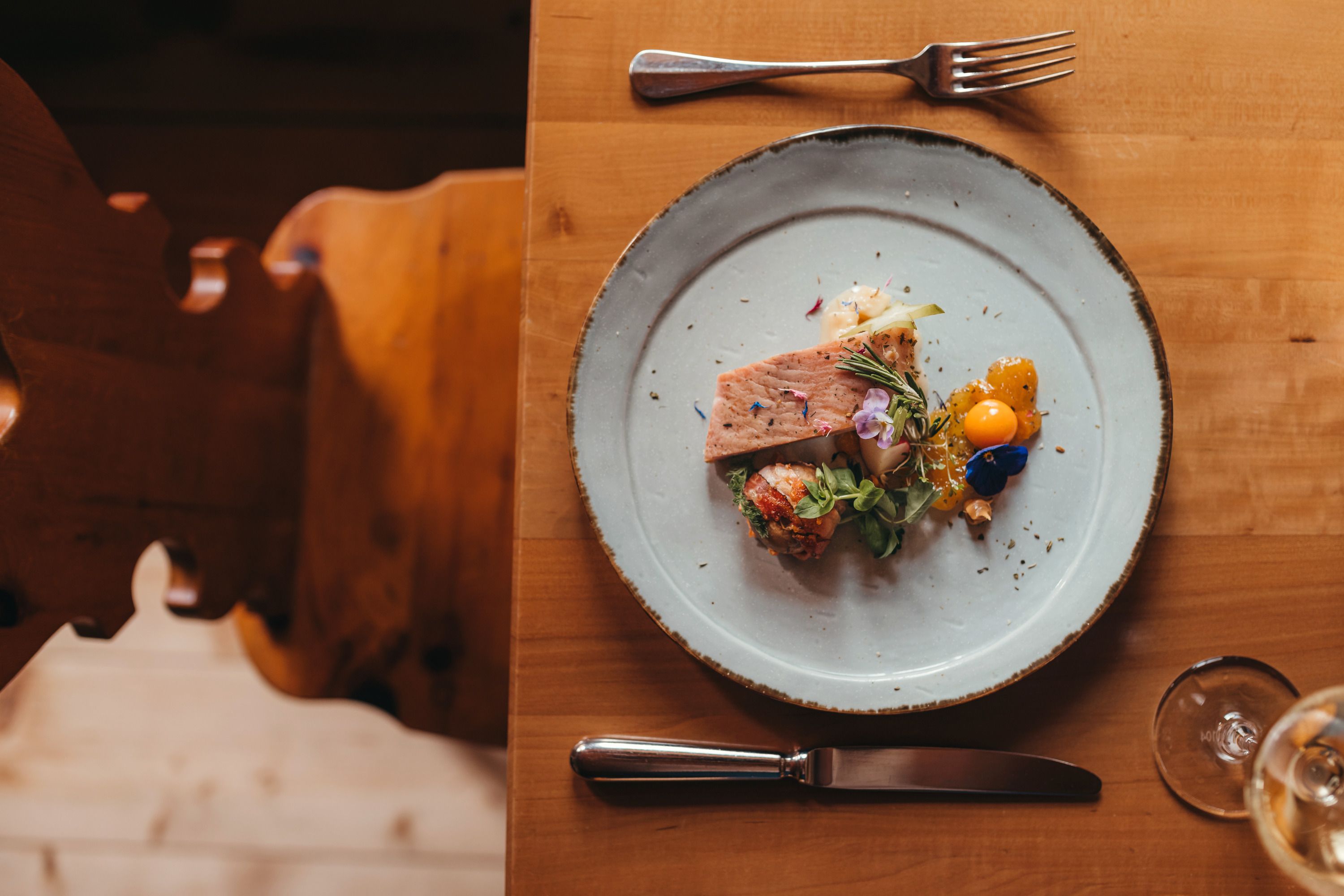Ein Teller mit geräuchertem Edelwelsfilet und Sellerie-Erdnusssalat, dekoriert mit essbaren Blüten, auf einem Holztisch.
