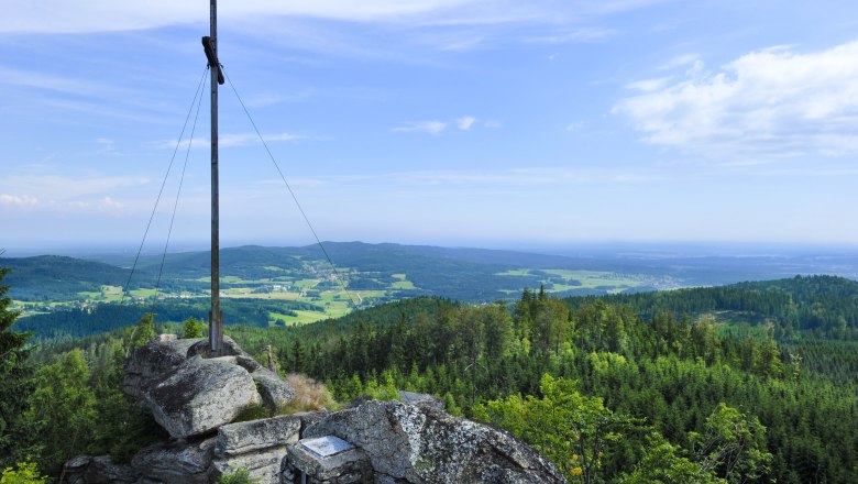 Blick vom Gipfel des Nebelsteins über eine grüne Landschaft mit Wäldern und Feldern, im Vordergrund ein Gipfelkreuz.