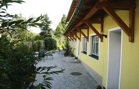 Gepflasterter Hof mit gelbem Geb&auml;ude und Gartenm&ouml;beln.